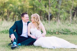 A couple in wedding attire lies on grass outdoors during a romantic countryside photoshoot.