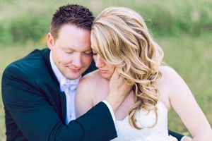 A romantic embrace between a couple in wedding attire sitting outdoors with soft natural lighting.