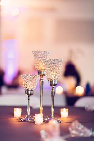 Crystal votive candle holders sparkle with tealights on an elegant reception table in soft romantic lighting.