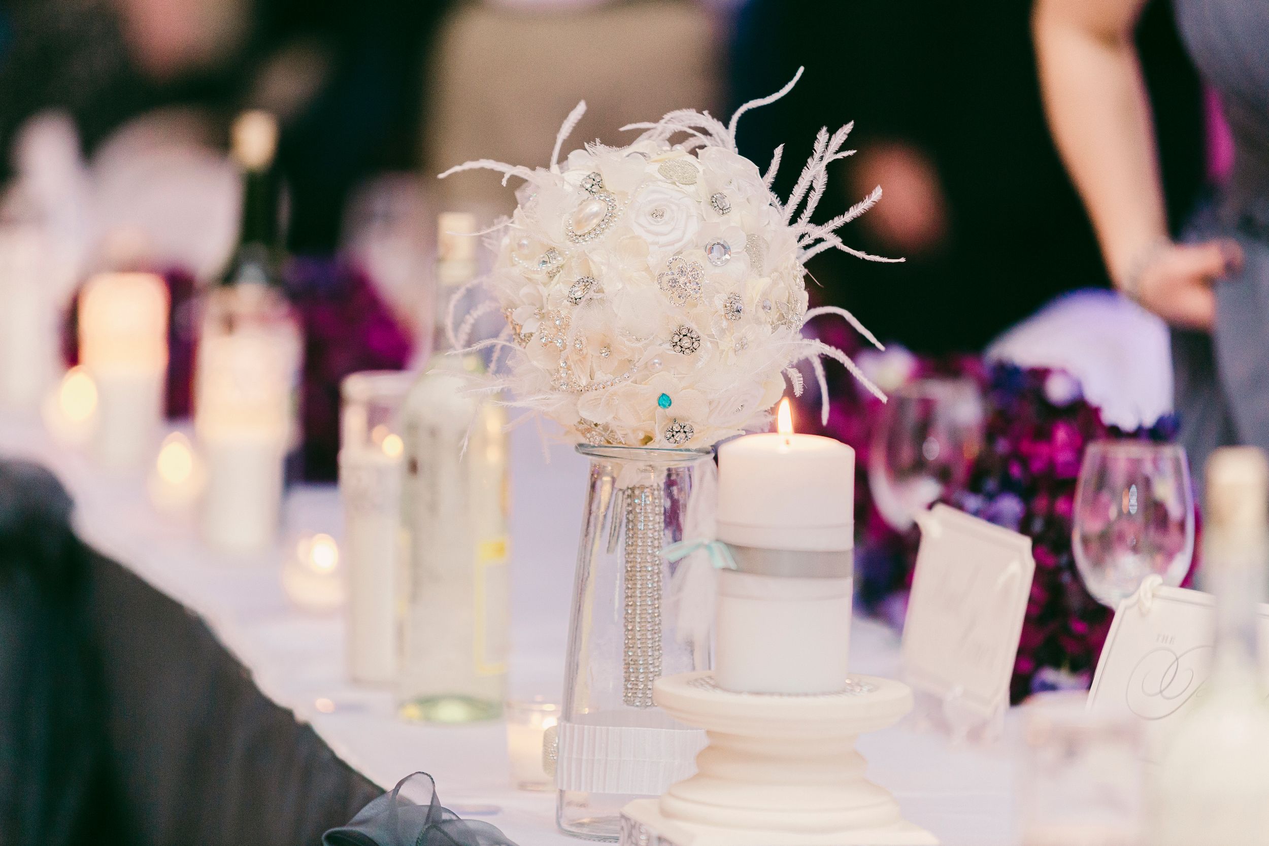 Elegant white feathered centerpiece decoration on a formal dining table with glowing candles and wine glasses.
