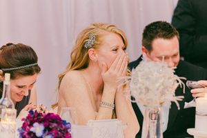 Emotional reactions during wedding reception speeches with purple floral bouquet on table.