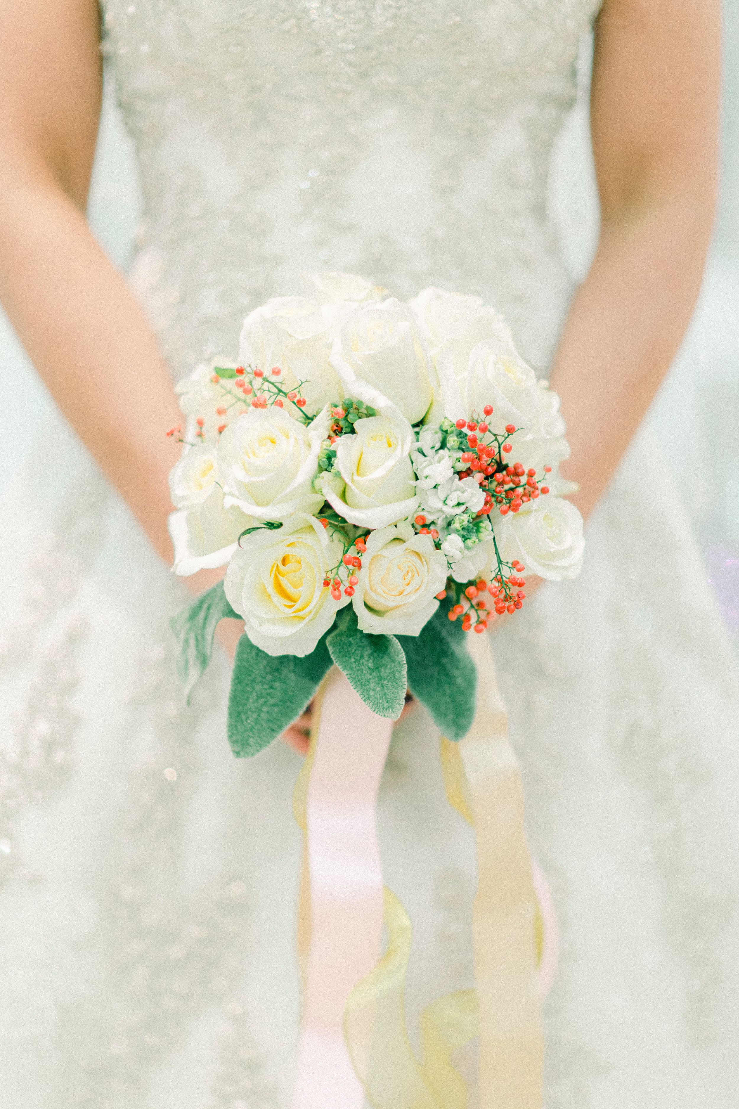 Three bridal bouquets with white roses, peach accents and pink ribbons are held against a light background.