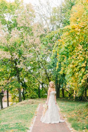 A tranquil autumn path lined with yellow and green trees features a white gown against the natural backdrop.