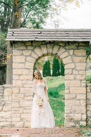 Stone archway with shingled roof surrounded by lush greenery in an elegant garden setting.