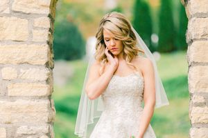 A serene bridal portrait in natural light showing an elegant lace wedding dress against a stone archway backdrop.