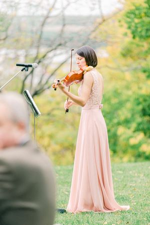 A violinist in a blush pink gown performs outdoors with sheet music stand during an autumn performance.