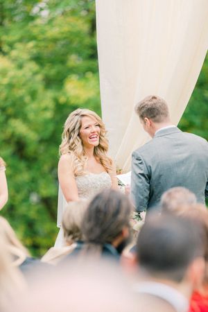 Joyful moment captured during outdoor wedding ceremony under white draping with guests looking on.