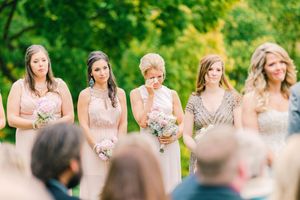 Bridesmaids hold white bouquets while standing in a line during an outdoor wedding ceremony.
