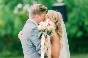 A couple shares a tender kiss during their wedding ceremony in a lush green outdoor garden setting.