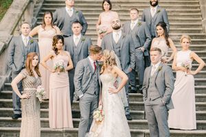 Wedding party in gray suits and blush pink dresses poses on grand stone stairs outdoors.