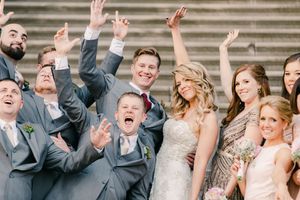 A joyful wedding party celebrates on the stone steps outside, with everyone raising their arms in excitement.