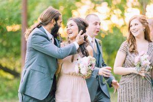 Wedding party members share a candid laugh together outdoors with bouquets during golden hour.