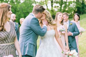 A couple shares their first kiss as newlyweds while their wedding party looks on during an outdoor ceremony.