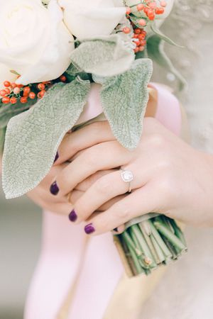 Close-up of hands holding white and coral flower bouquet with silver engagement ring and purple nail polish.