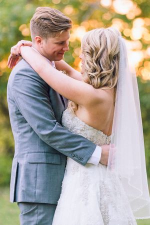 Newly married couple embraces outdoors with warm golden bokeh lights in background during sunset.