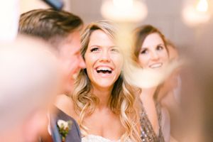 Joyful bride laughing during candid wedding moment with blurred background and warm lighting.