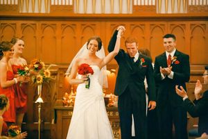 Wedding party members dance joyfully in formal attire inside an elegant ballroom with warm amber lighting.