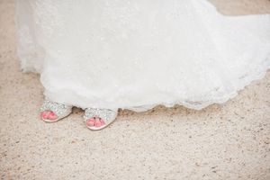 The unique embellishment on a white wedding dress can be seen in detail against a sandy, textured background.