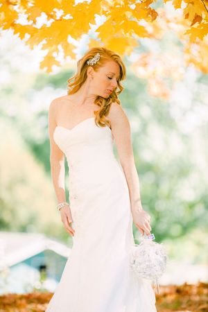 A strapless white wedding dress is showcased against vibrant autumn foliage creating a romantic fall scene.