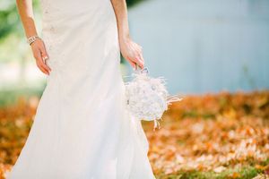 A flowing white wedding dress and bouquet captured against a backdrop of autumn leaves by the water.