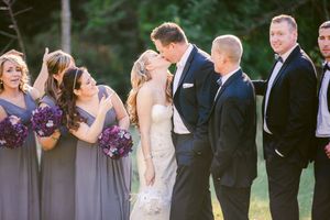 Wedding party gathers outdoors in purple and grey attire during sunset ceremony.