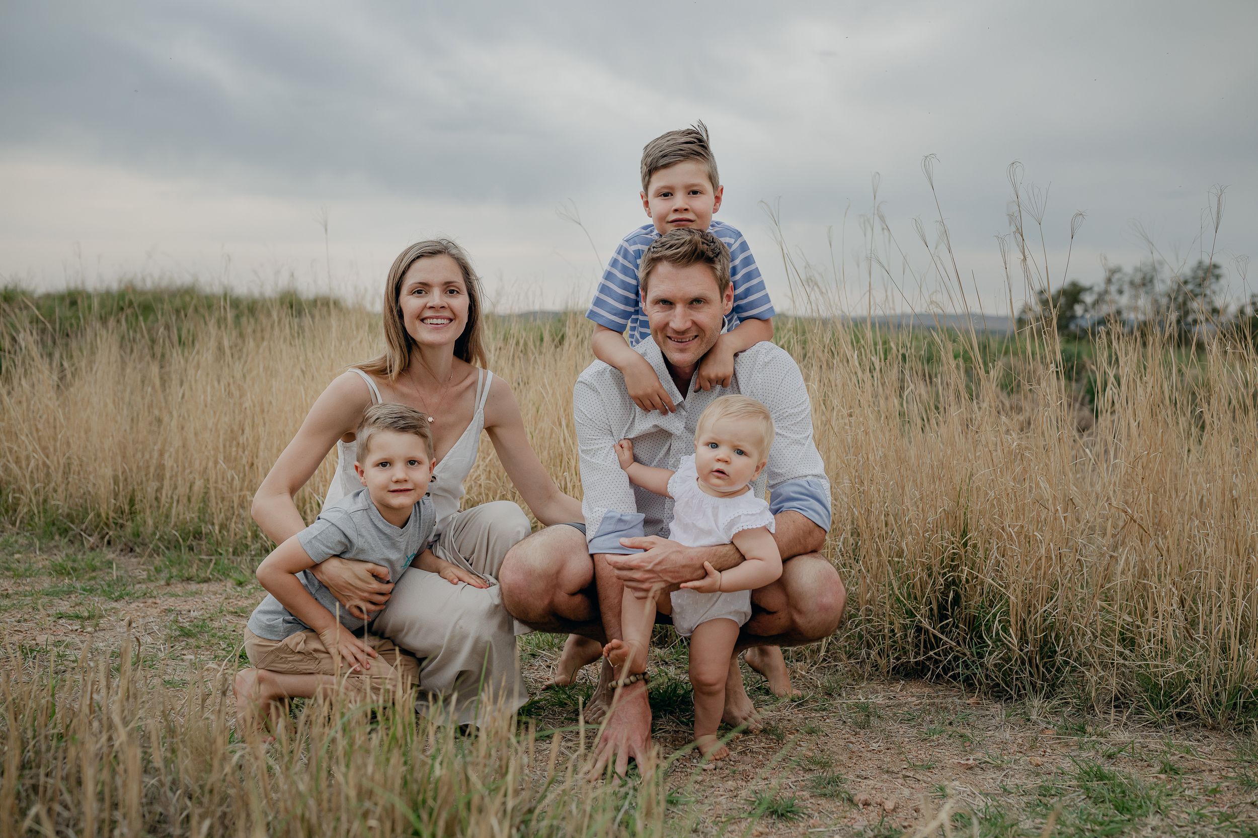 Casual family portrait in field of tall grass during overcast day.