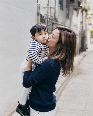 A touching family moment standing against an urban wall with soft lighting and casual style.