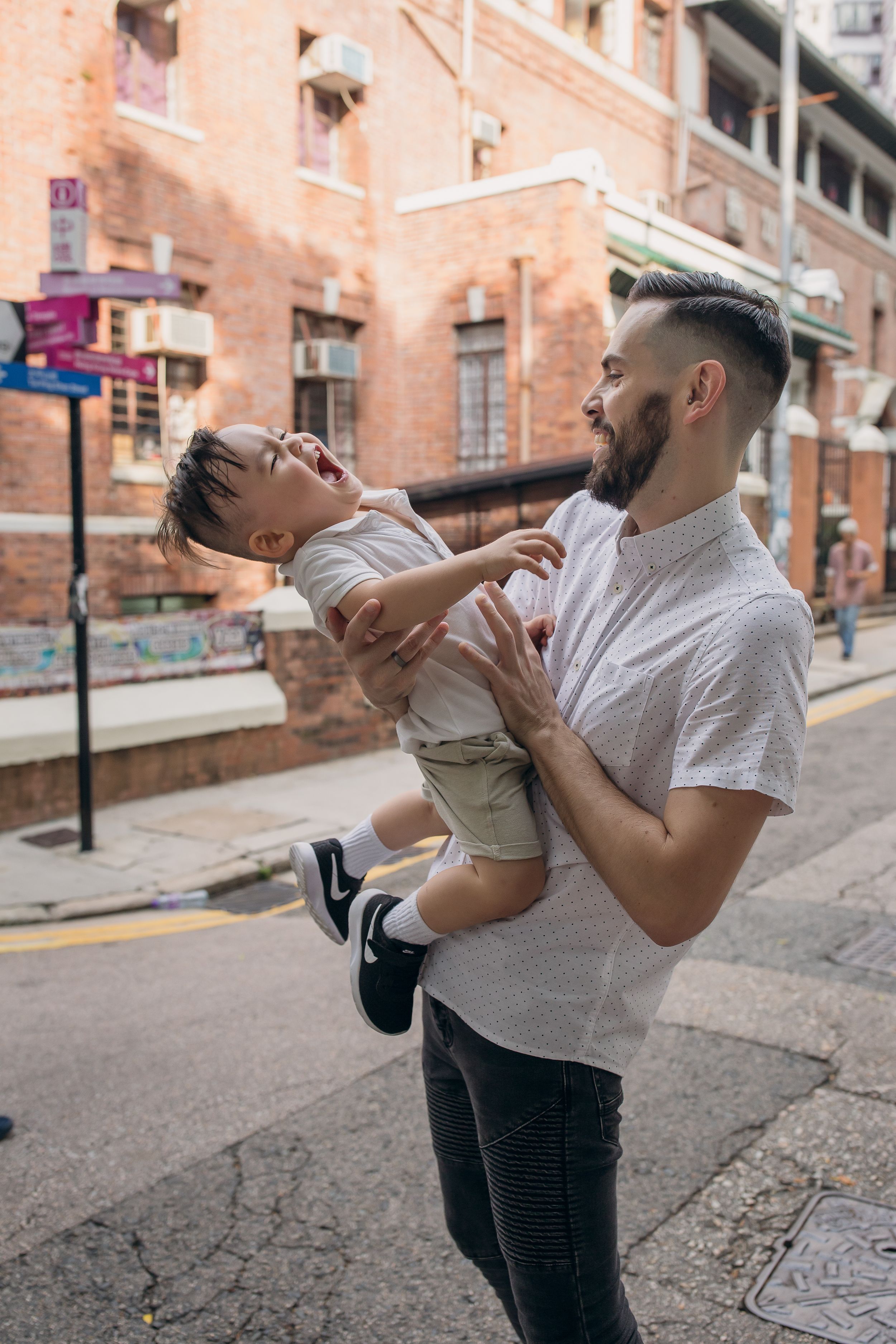 A playful interaction between adult and child on an urban street with brick buildings.
