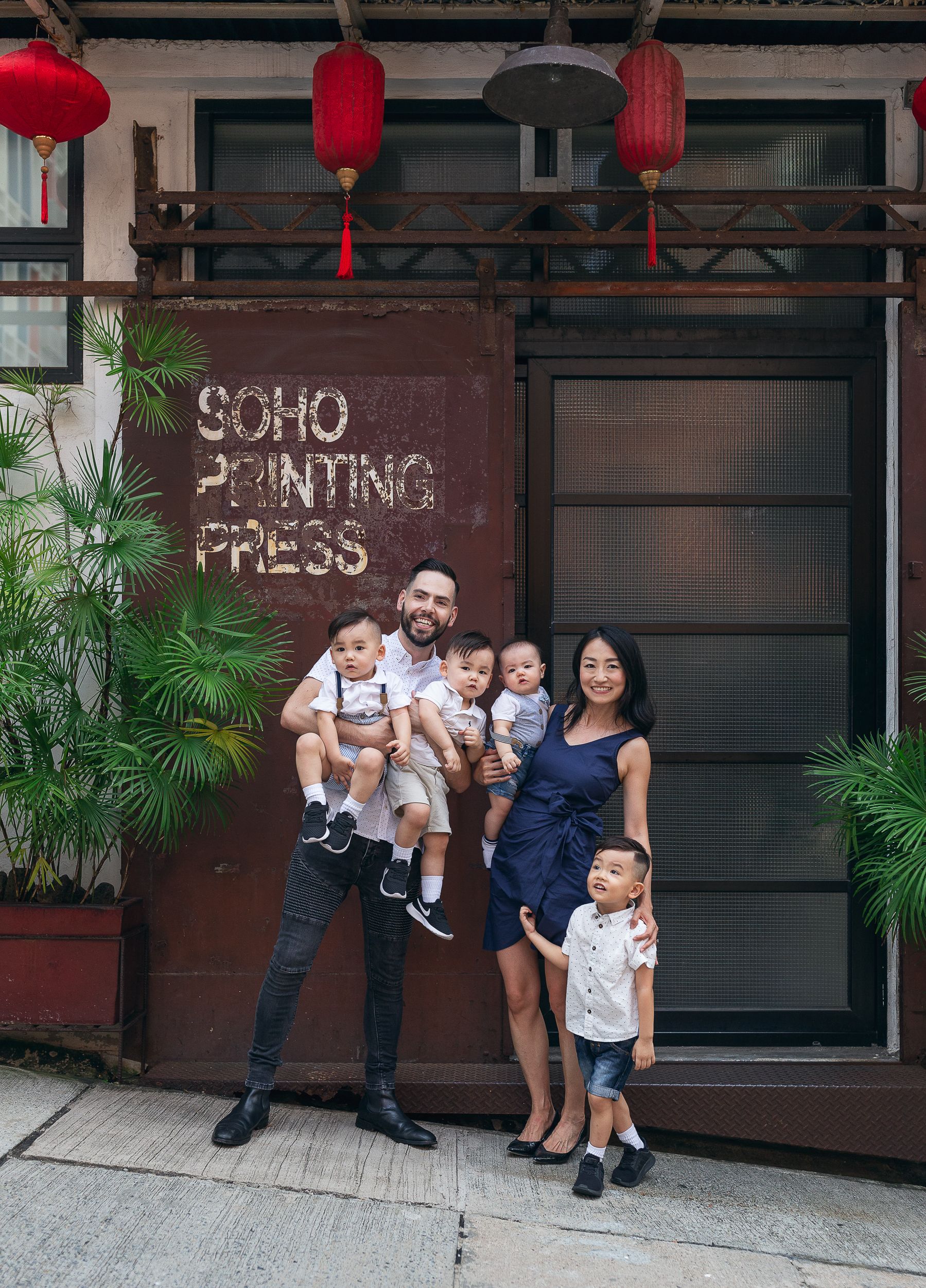 A family poses outside the Soho Printing Press building with red lanterns overhead.