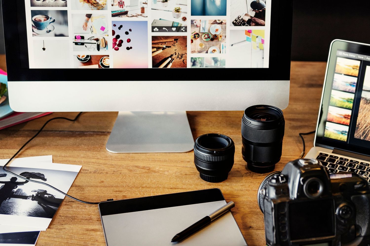 Professional photography equipment and office supplies arranged on a wooden desk with natural lighting.