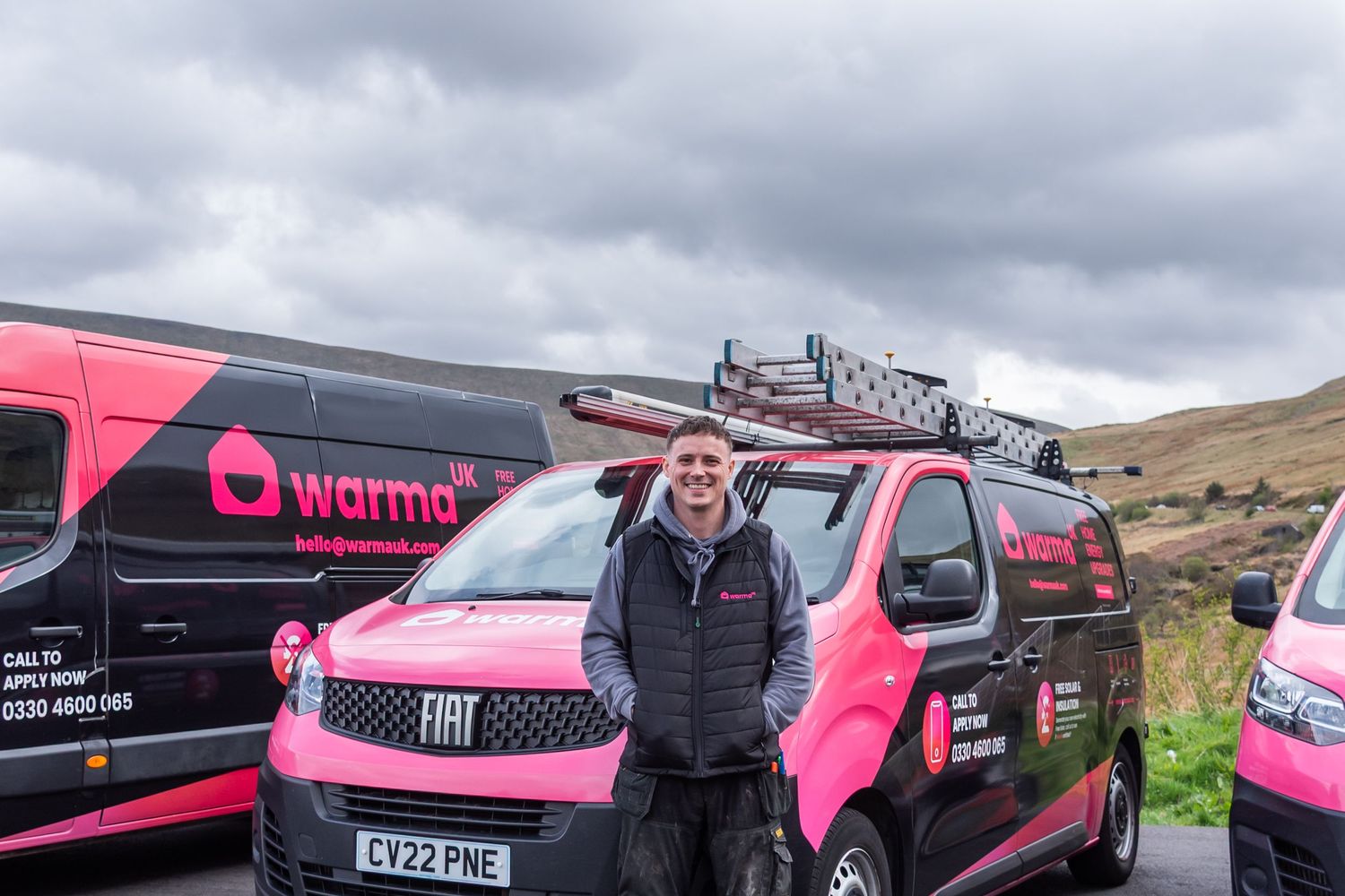 Fleet of pink branded vehicles parked along a rural road with hills in background.