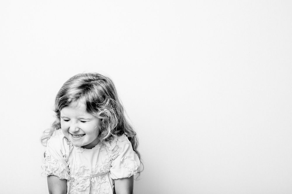 Black and white photo of a laughing child in a vintage-style dress against white background.