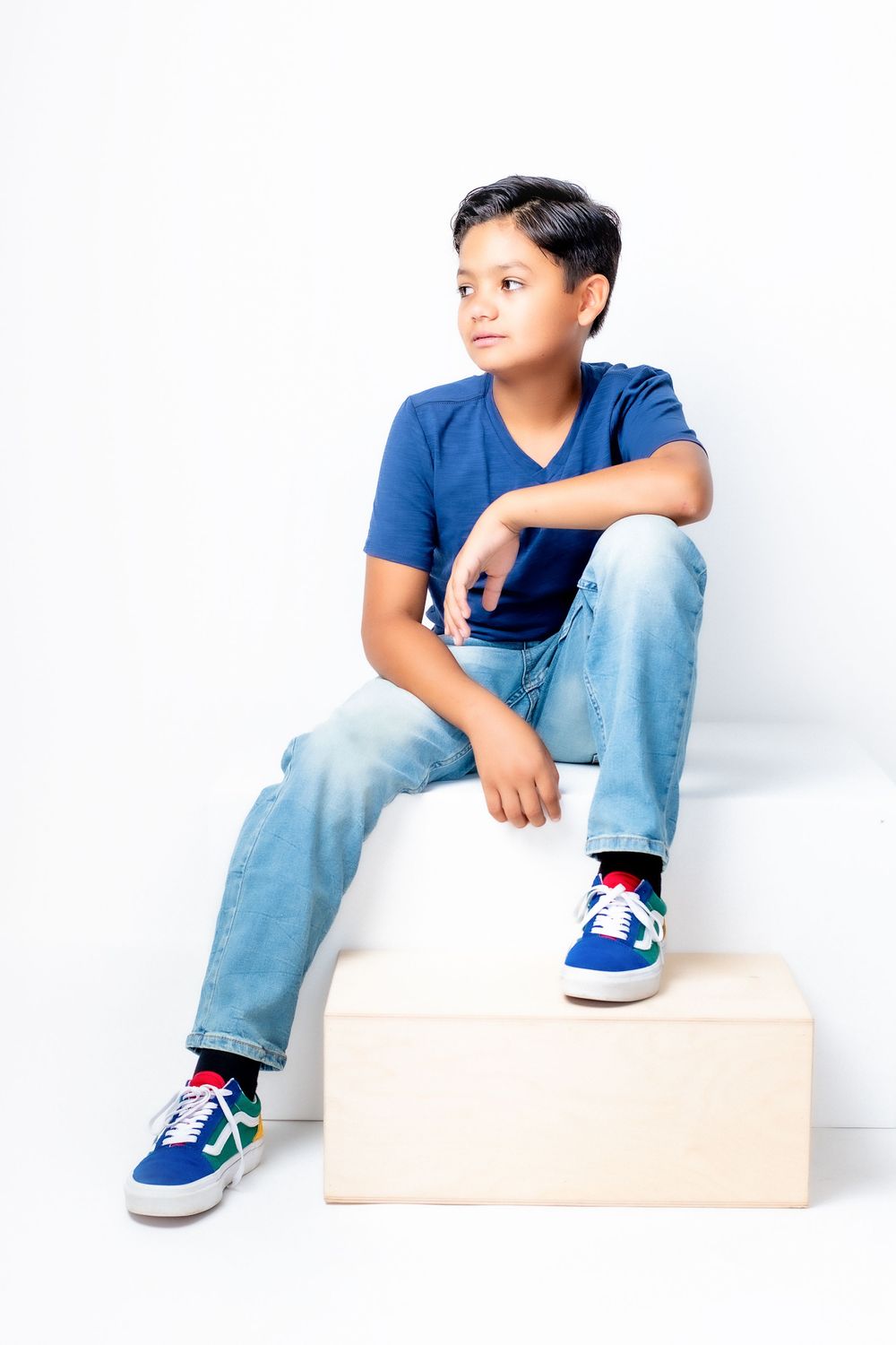 A child in a blue shirt and jeans sits on white boxes in three progressive poses looking sideways and upward.