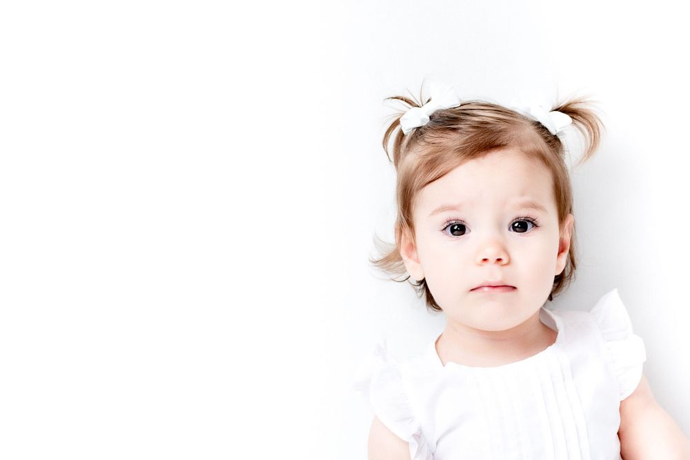 Sweet portrait of a toddler in white dress with pigtails against white background.