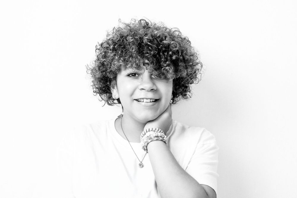 Black and white portrait of person with curly hair wearing a white shirt and smiling at the camera.