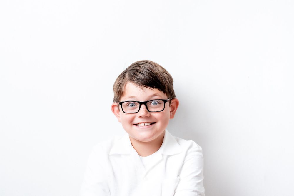 Close-up portrait of a smiling youth in glasses and white shirt against white background.