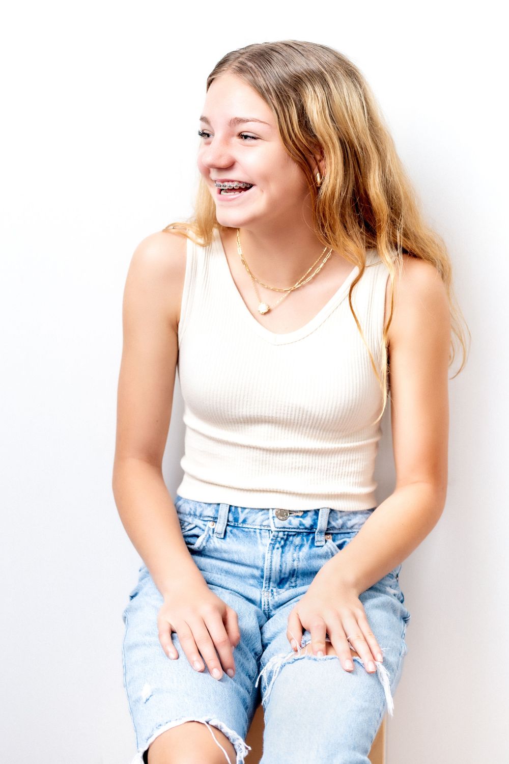 Candid portrait of a teen laughing in white tank top and distressed jeans.