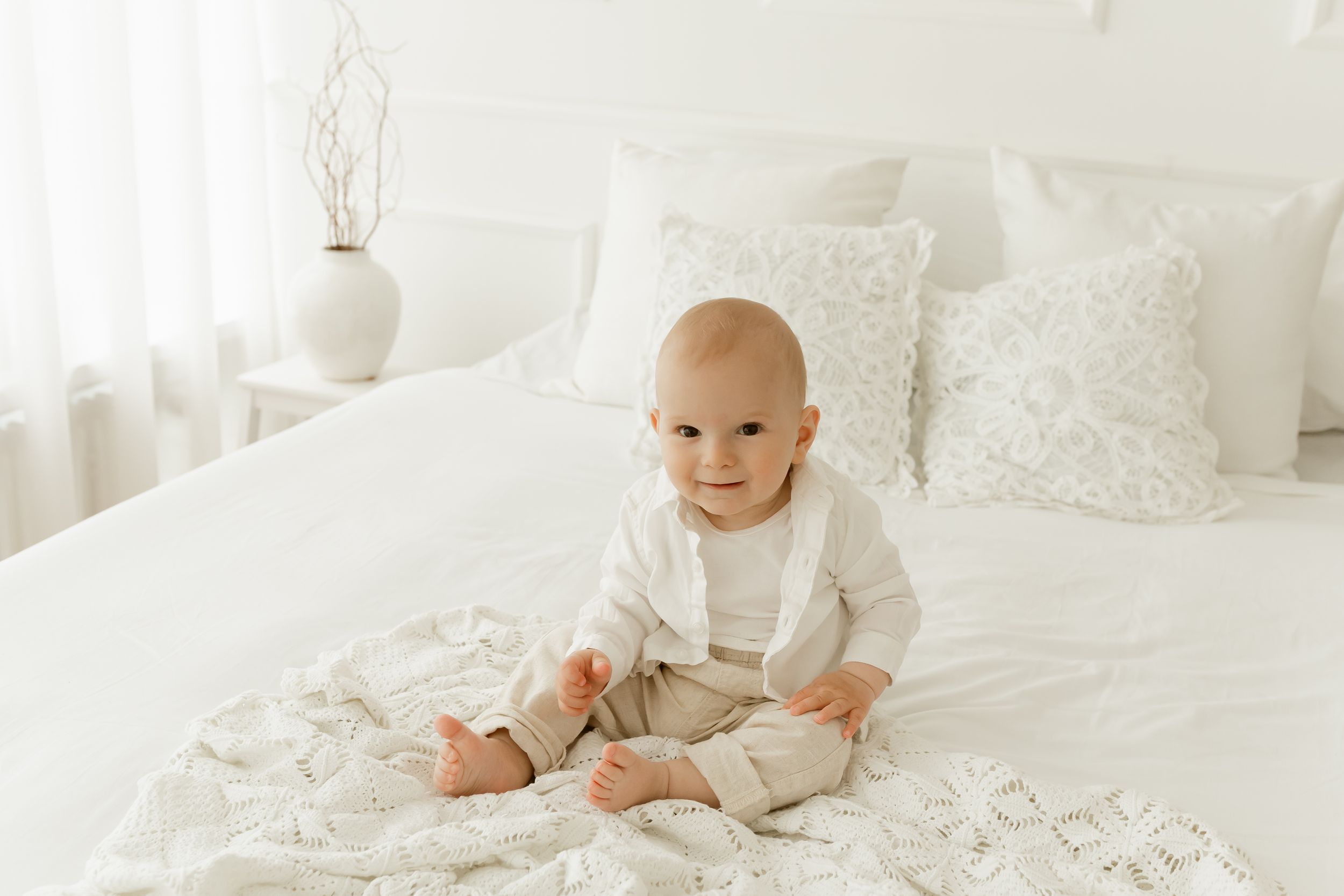 Baby in white onesie crawls and plays on white bedding with floral pattern sheets.
