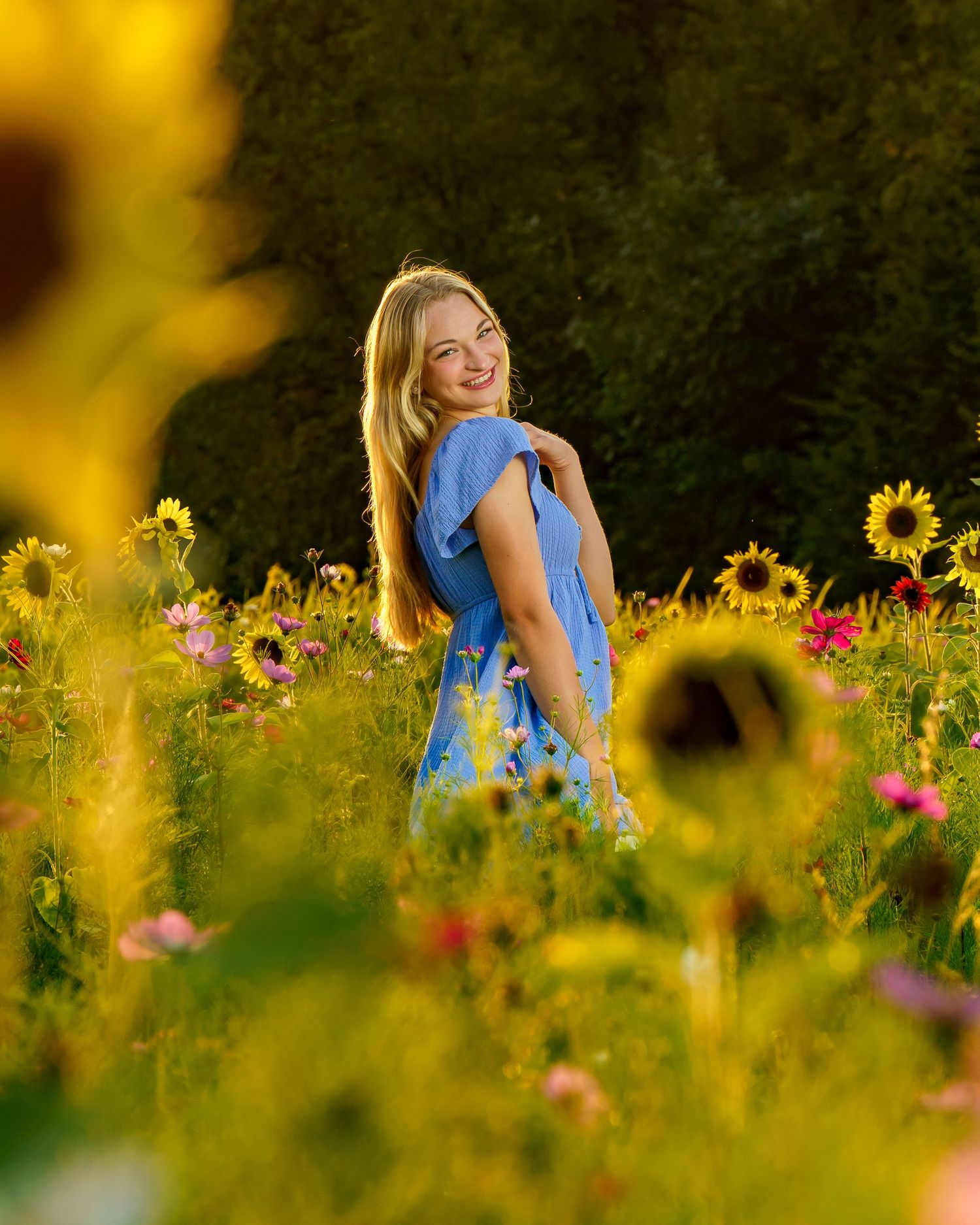A blue dress-clad figure stands in a vibrant summer garden filled with colorful sunflowers and wildflowers on a sunny day.