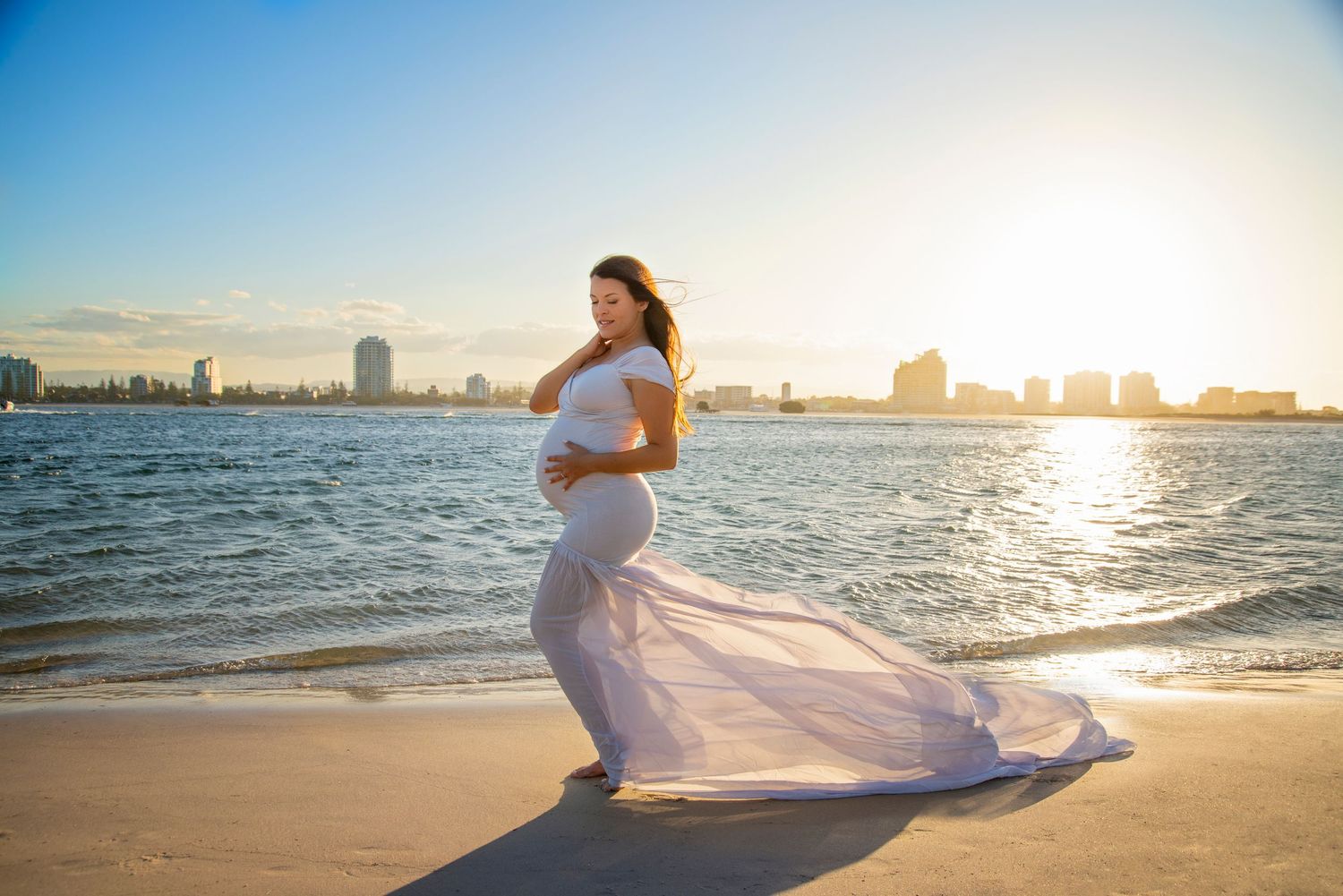 pregnant lady in a tight fitting grey mermaid style train dress with gold coast skyline in the background