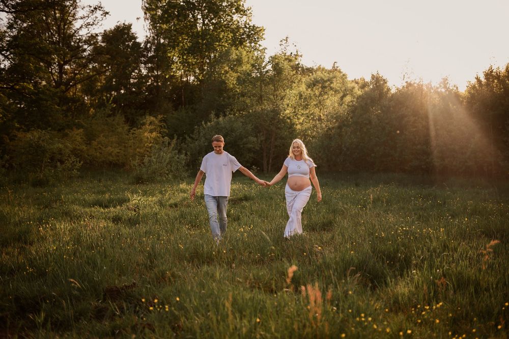 Two figures walk hand in hand through a sunlit meadow at golden hour as sunbeams filter through trees in the background.
