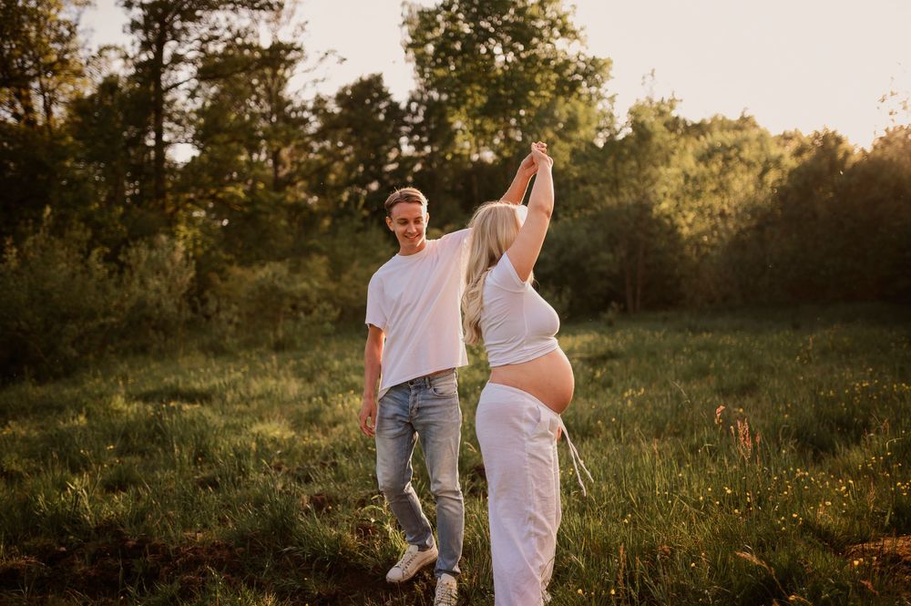 Couple dancing together in a sunlit field during maternity photo session.