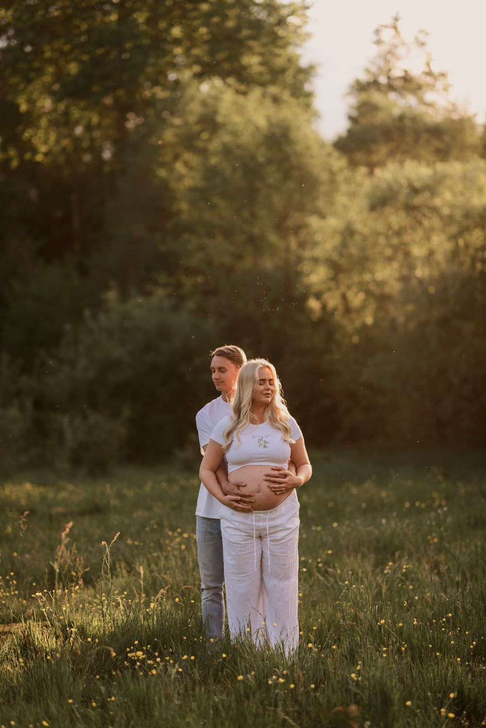 Intimate maternity portrait of couple embracing in a golden-lit field at sunset.