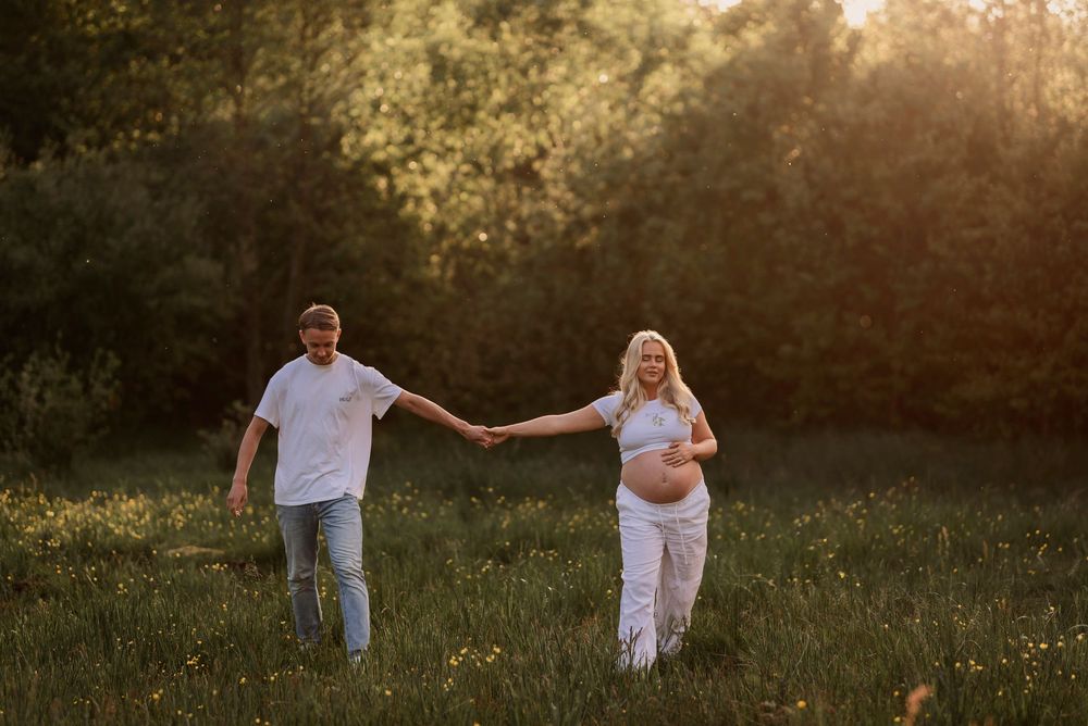 A couple holds hands while walking through a sunlit meadow at golden hour.