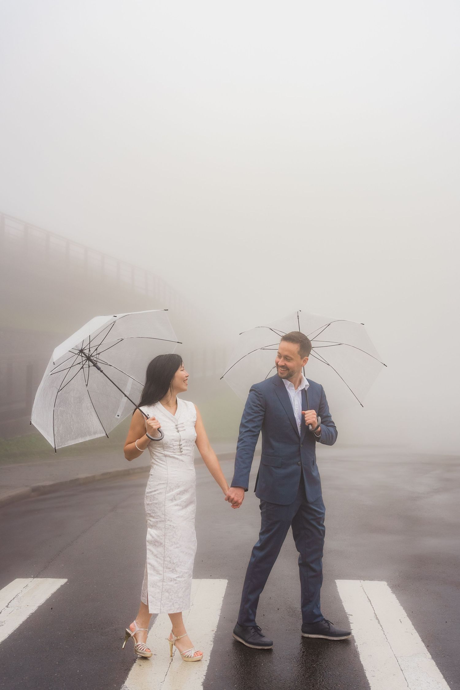 A couple embraces on a foggy path with wooden fencing, as one person lifts the other in a romantic moment.