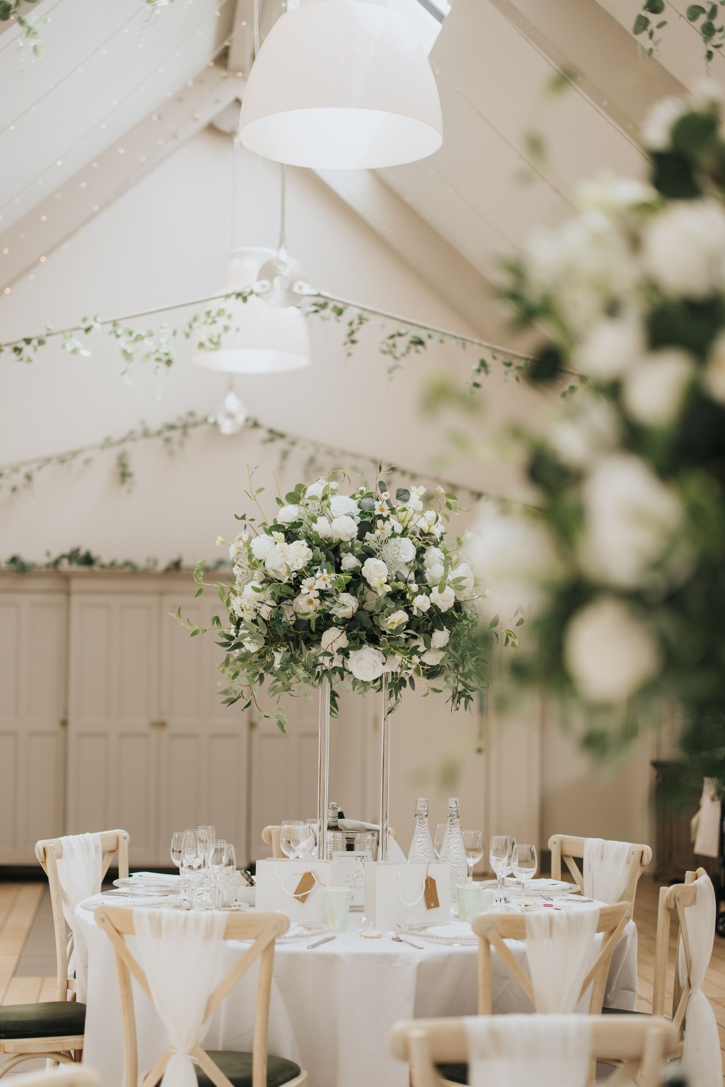 White reception tent with round tables elegantly decorated with floral arrangements and white linens for wedding celebration.