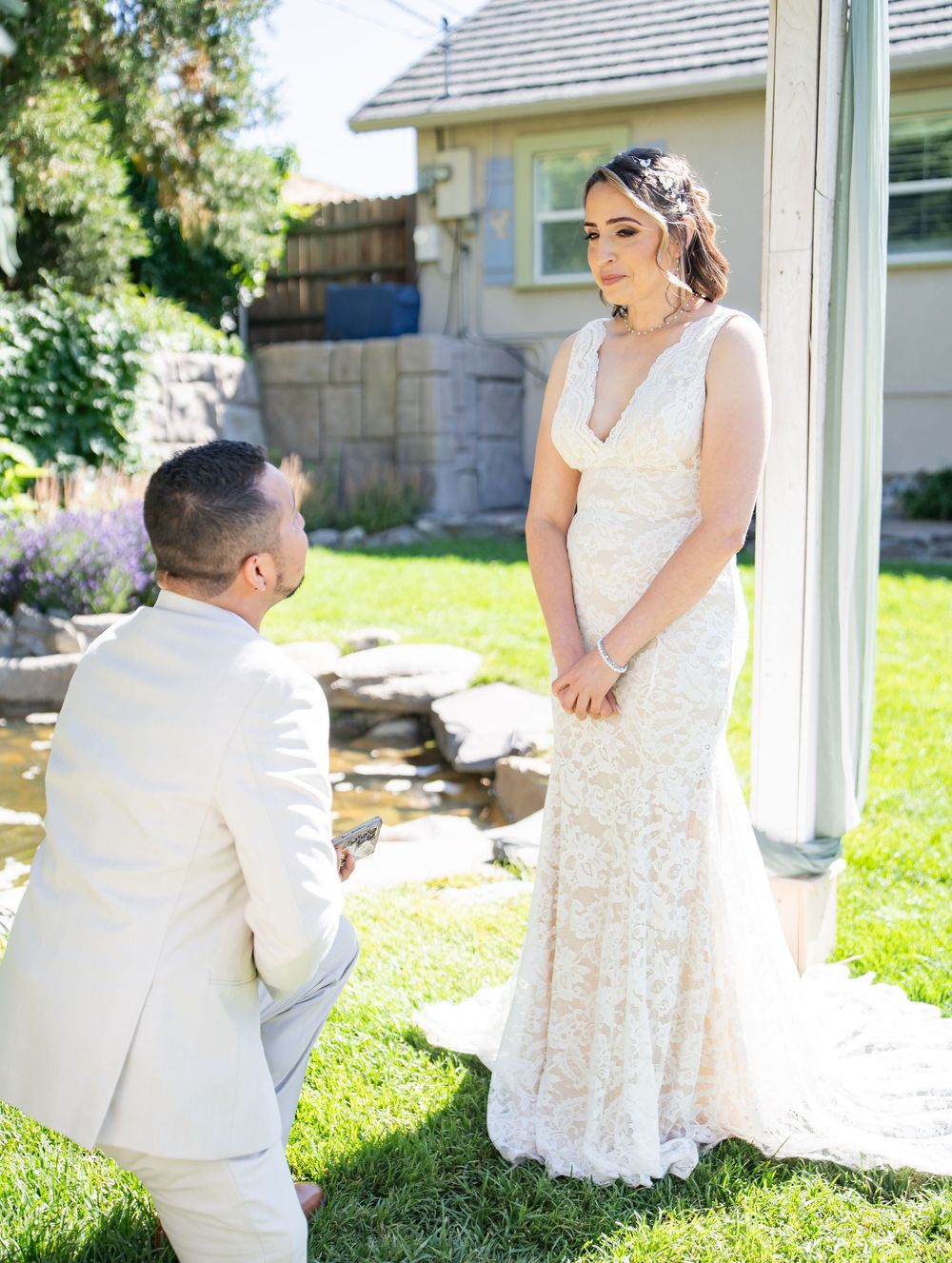 A couple shares a joyful moment on their garden wedding day, with the person in white proposing to their partner.