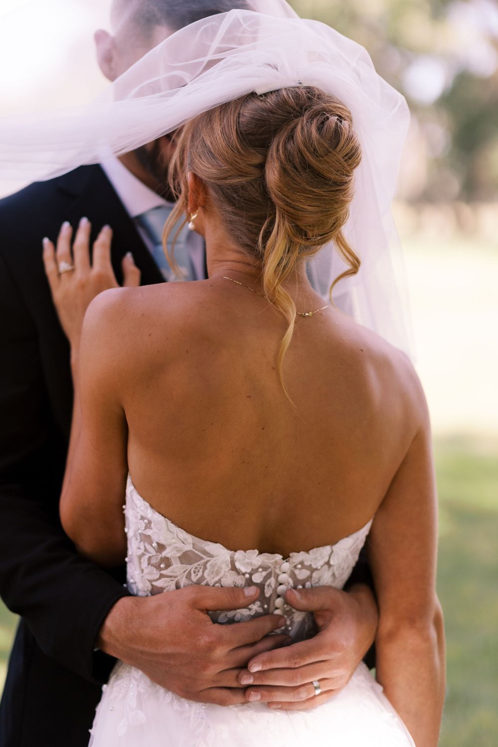 Close-up of bride and groom embracing, showing bride's detailed lace back wedding dress and elegant updo hairstyle.
