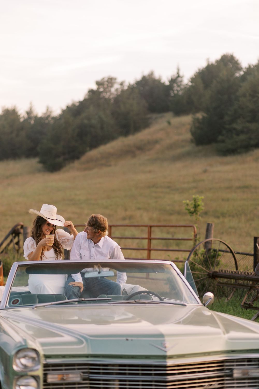 Couple sitting in vintage Cadillac convertible in rural setting.