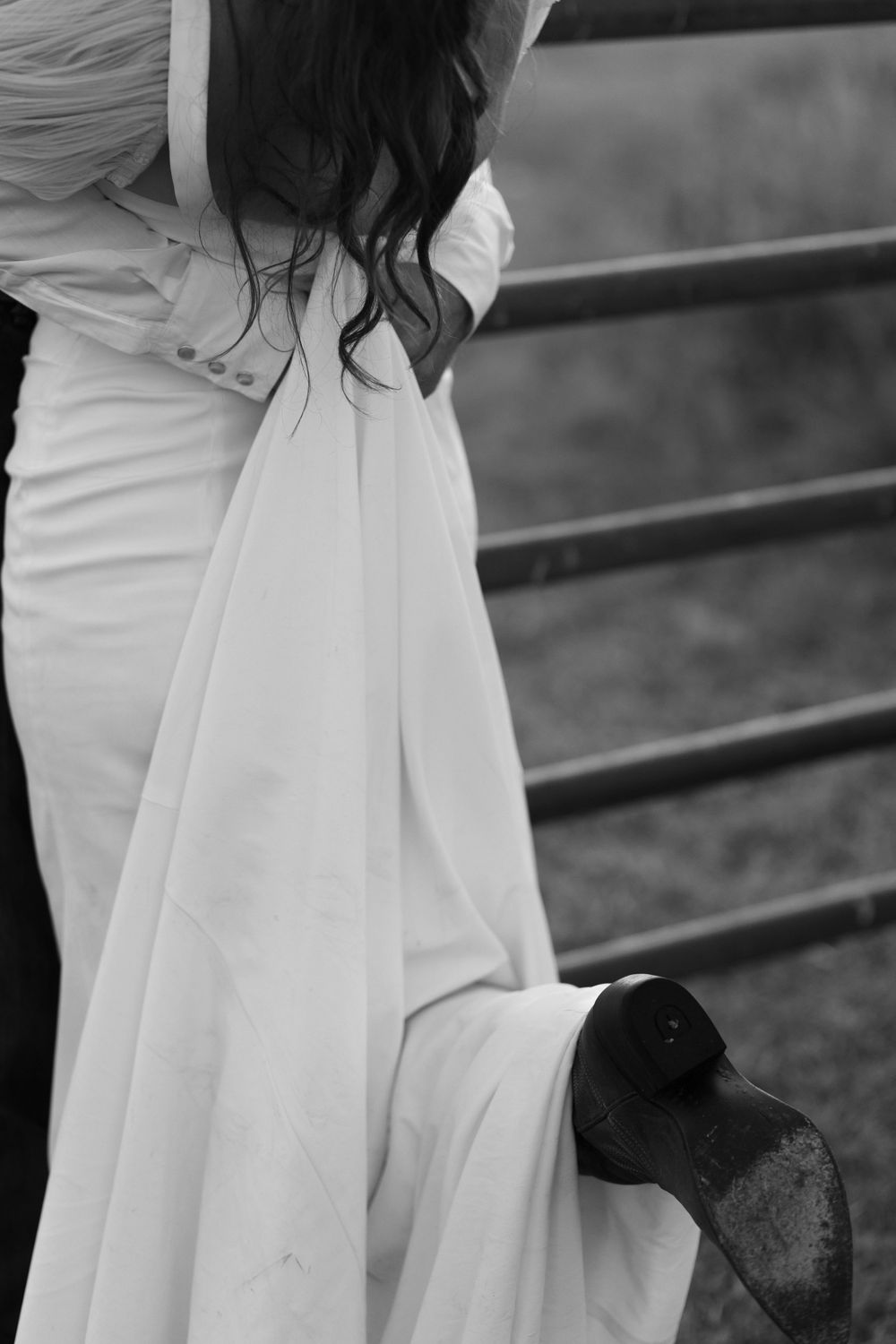 Close-up of flowing white wedding dress against metal fence rails.